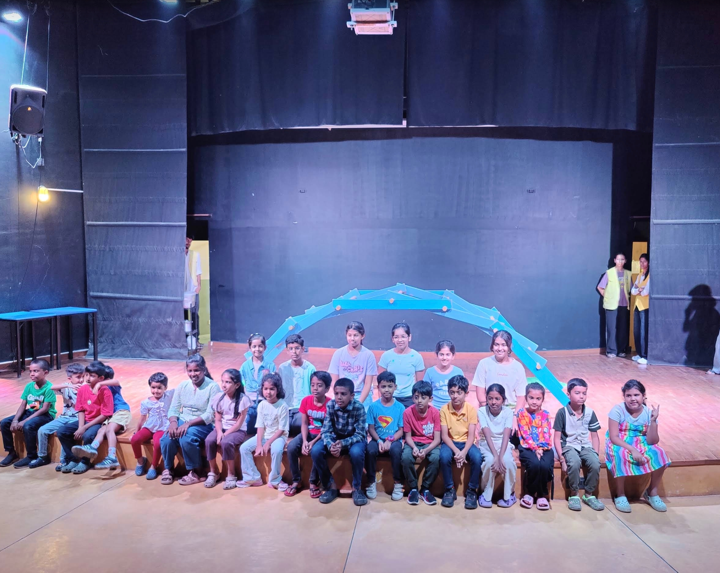 Children seated on the auditorium stage with a blue arch